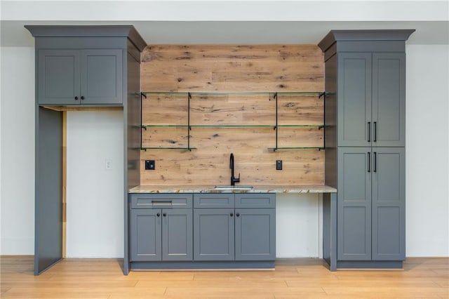 bar featuring light wood-type flooring, indoor wet bar, and a sink