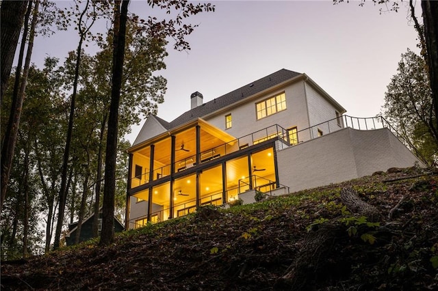 back of property at dusk featuring a chimney, ceiling fan, and a balcony