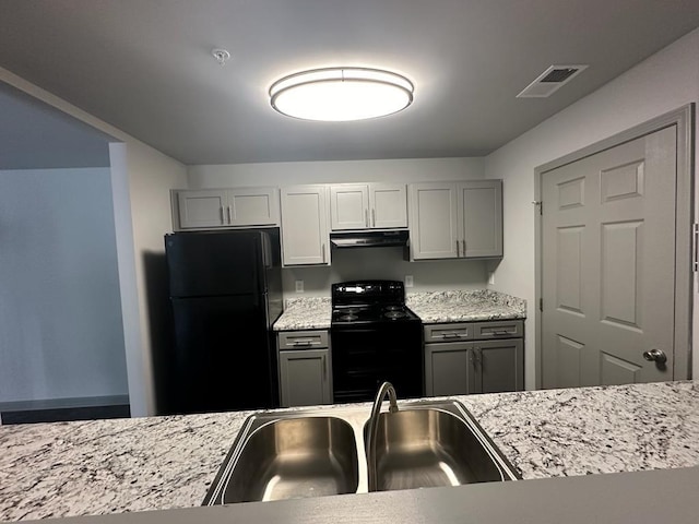 kitchen with light stone countertops, sink, gray cabinetry, and black appliances