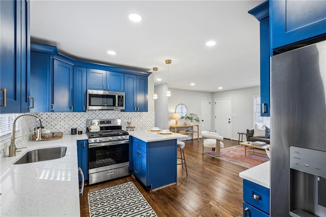 kitchen with appliances with stainless steel finishes, blue cabinets, sink, a kitchen bar, and hanging light fixtures