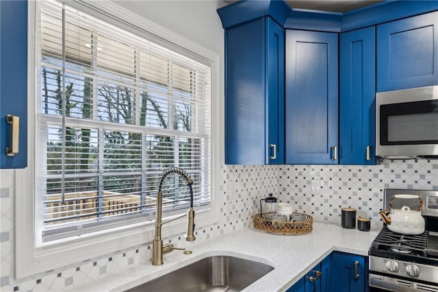 kitchen featuring blue cabinets, sink, light stone counters, stainless steel appliances, and decorative backsplash