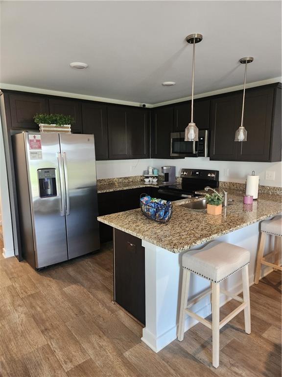 4839 Station Ln, Union City, GA 30349 - kitchen featuring stainless steel appliances, light wood-style flooring, light stone counters, dark cabinets, and hanging light fixtures