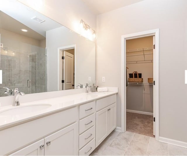 full bathroom with visible vents, double vanity, a stall shower, a sink, and a walk in closet