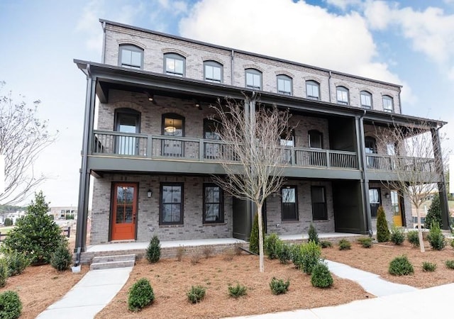 view of property featuring brick siding, covered porch, and a balcony