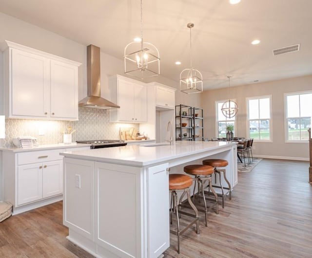 kitchen featuring visible vents, a sink, white cabinetry, wall chimney range hood, and backsplash