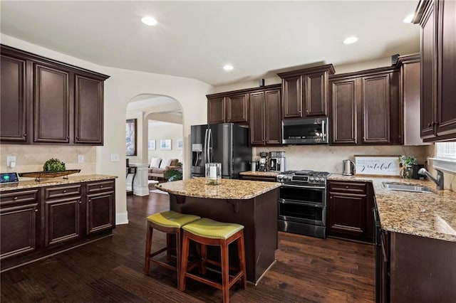 kitchen with light stone counters, a breakfast bar area, appliances with stainless steel finishes, a sink, and a kitchen island