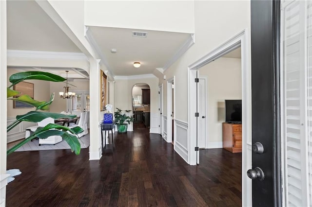 entrance foyer with dark wood-style floors, arched walkways, a notable chandelier, visible vents, and ornamental molding