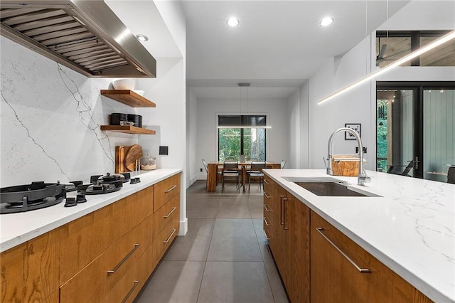 kitchen featuring island range hood, decorative light fixtures, sink, dark tile patterned floors, and light stone counters