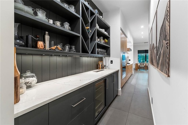 bar with sink, light stone counters, tile patterned floors, beverage cooler, and stainless steel oven