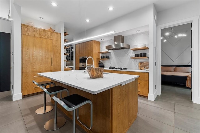 kitchen with wall chimney range hood, tasteful backsplash, white gas stovetop, an island with sink, and a kitchen bar