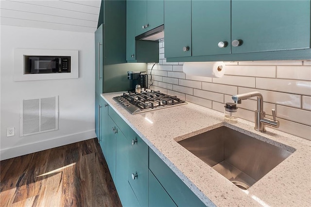 kitchen with sink, dark wood-type flooring, light stone counters, stainless steel gas cooktop, and decorative backsplash