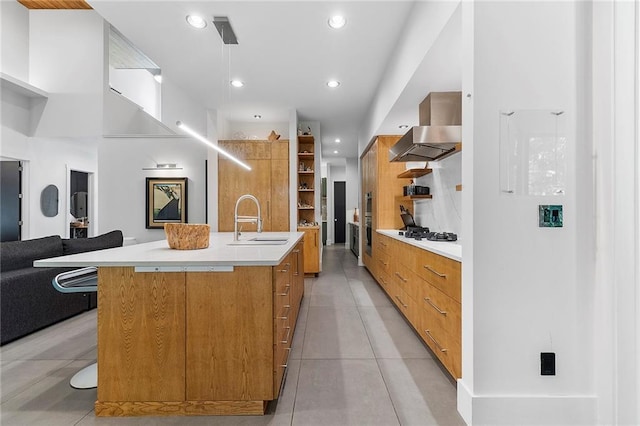 kitchen with sink, a large island with sink, light tile patterned floors, wall chimney range hood, and white gas cooktop