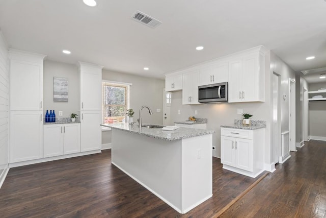 kitchen with white cabinetry, a kitchen island with sink, sink, and light stone counters