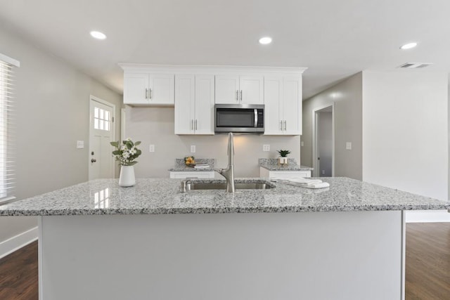 kitchen featuring light stone counters, white cabinets, sink, and a large island with sink