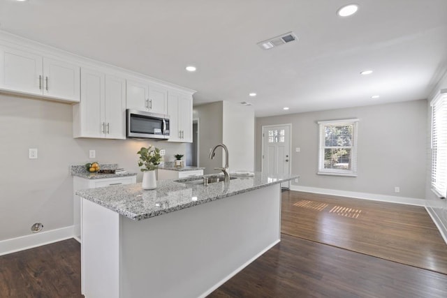 kitchen with white cabinetry, an island with sink, sink, light stone counters, and dark wood-type flooring