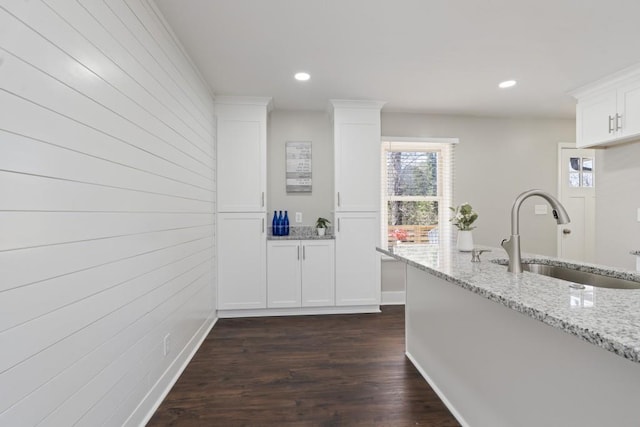 kitchen with dark hardwood / wood-style floors, light stone countertops, sink, and white cabinets