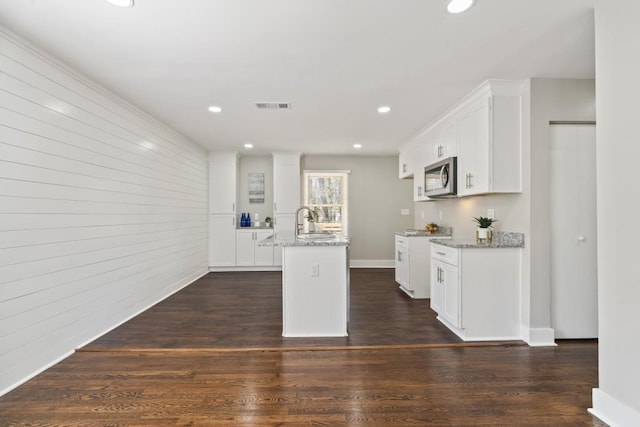 kitchen with white cabinetry, light stone countertops, dark wood-type flooring, and an island with sink