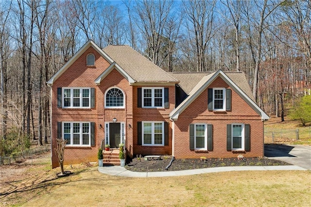 colonial house with brick siding, a shingled roof, a front lawn, and fence