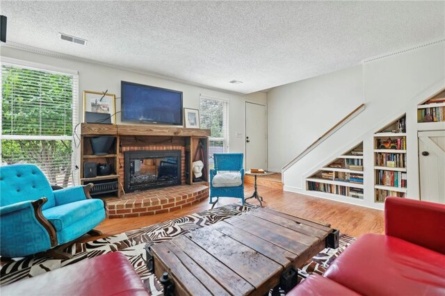 living room featuring a textured ceiling, wood-type flooring, a brick fireplace, and plenty of natural light