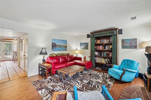 living room with crown molding, a textured ceiling, light wood-type flooring, and french doors