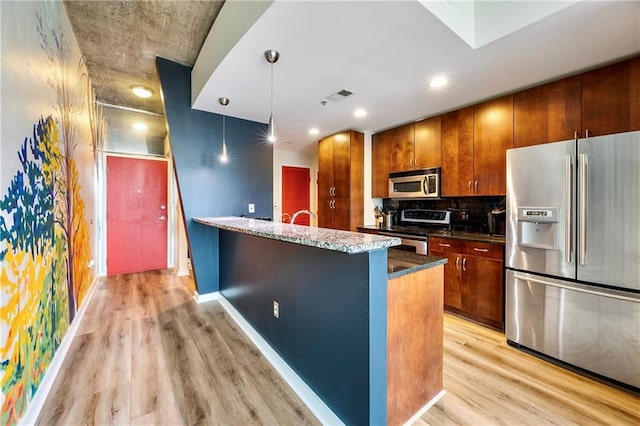 kitchen with tasteful backsplash, hanging light fixtures, stainless steel appliances, light hardwood / wood-style floors, and a kitchen island with sink