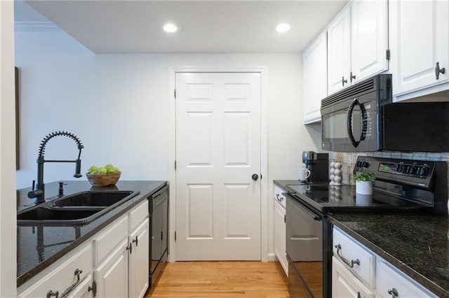 kitchen featuring light wood-style flooring, dark stone countertops, black appliances, white cabinetry, and a sink