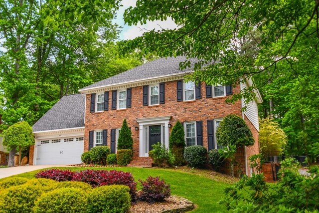 colonial house with brick siding, a garage, roof with shingles, and driveway