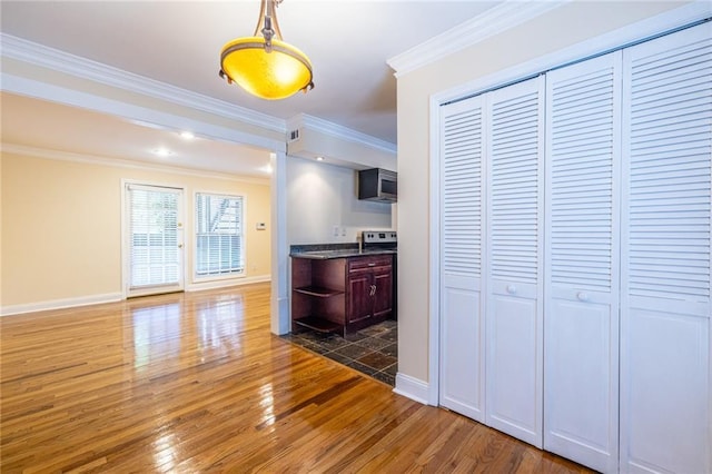 kitchen with hardwood / wood-style flooring, baseboards, stainless steel microwave, dark countertops, and crown molding