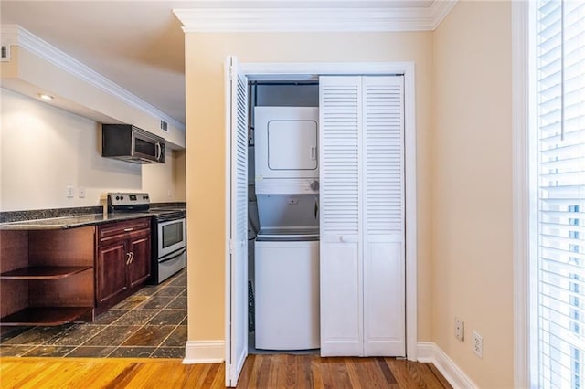 kitchen featuring stainless steel appliances, estacked washer and dryer, dark countertops, crown molding, and healthy amount of natural light