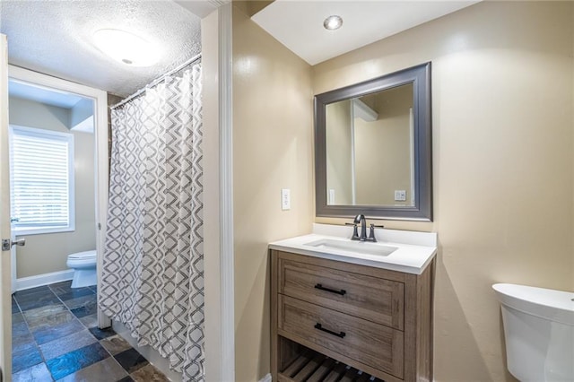 bathroom with toilet, vanity, baseboards, stone finish floors, and a textured ceiling
