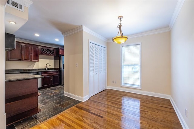 kitchen featuring dark countertops, a sink, ornamental molding, dark wood-style flooring, and baseboards