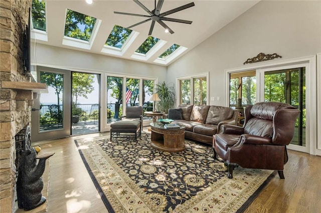 living area featuring high vaulted ceiling, a ceiling fan, wood finished floors, a skylight, and a fireplace