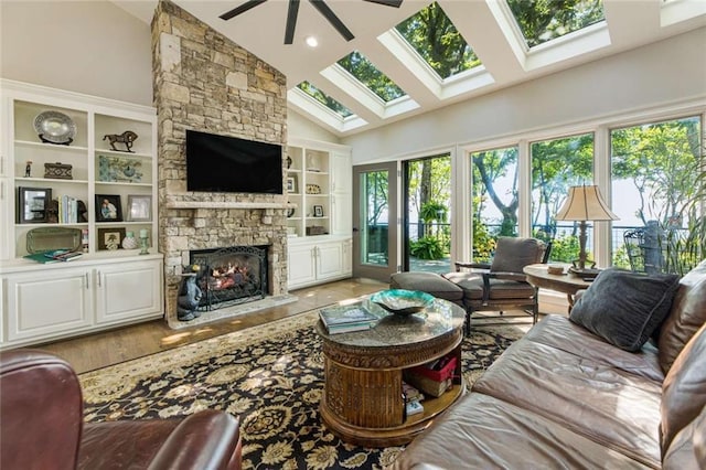 living room featuring a stone fireplace, a skylight, high vaulted ceiling, and ceiling fan