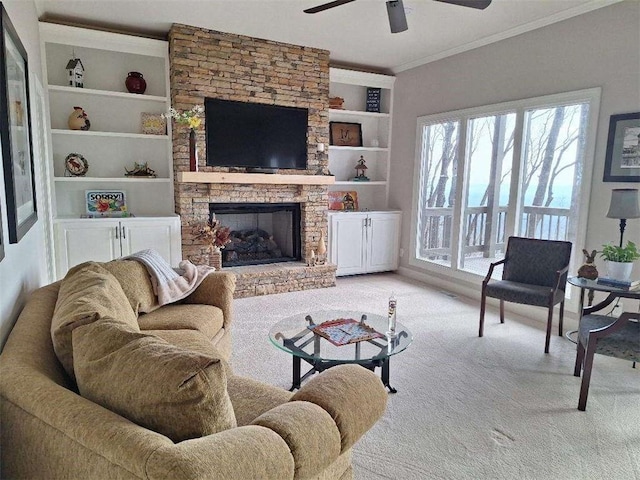 living room featuring ornamental molding, built in features, a stone fireplace, light colored carpet, and ceiling fan