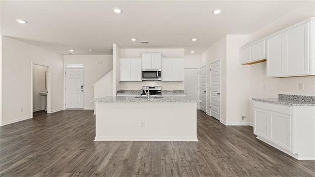 kitchen with appliances with stainless steel finishes, white cabinetry, light stone countertops, an island with sink, and dark hardwood / wood-style flooring