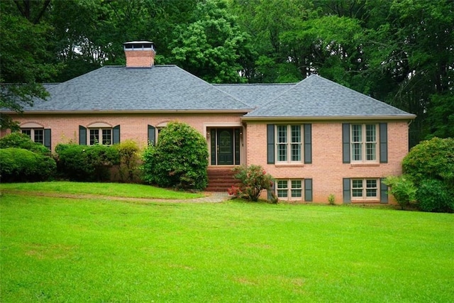 back of house featuring a yard, a shingled roof, a chimney, and brick siding