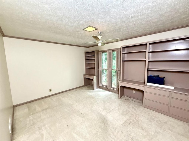 unfurnished office with a ceiling fan, carpet flooring, crown molding, baseboards, and built in desk