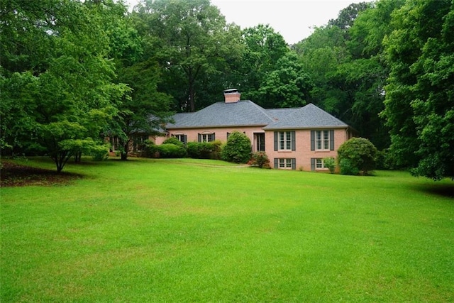 view of front of house with a front yard, a chimney, and a forest view