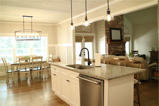 kitchen featuring white cabinets, sink, a brick fireplace, stainless steel dishwasher, and light stone counters