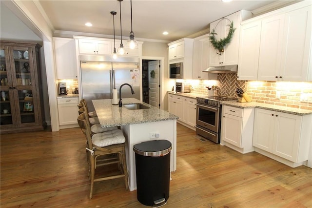 kitchen featuring built in appliances, an island with sink, white cabinetry, and sink