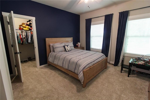 bedroom with a closet, a spacious closet, ceiling fan, and light colored carpet