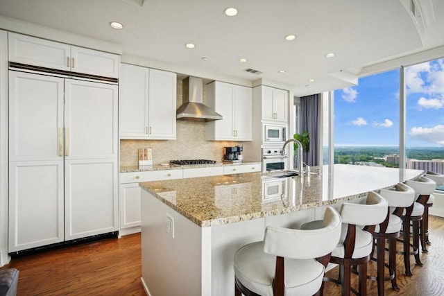 kitchen with wall chimney exhaust hood, white appliances, a sink, and dark wood-type flooring