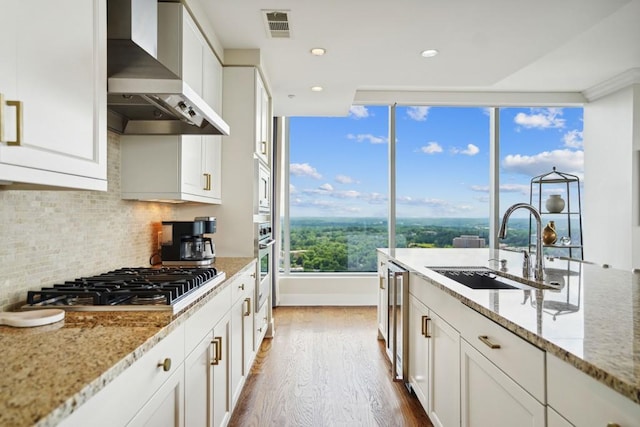 kitchen featuring wood finished floors, a sink, stainless steel appliances, wall chimney exhaust hood, and visible vents