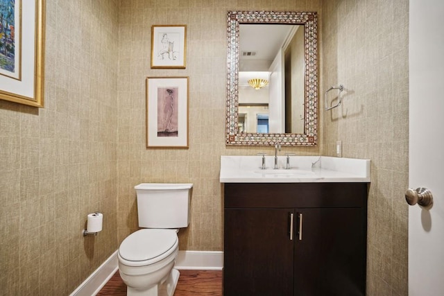 half bath with wood finished floors, vanity, baseboards, toilet, and visible vents