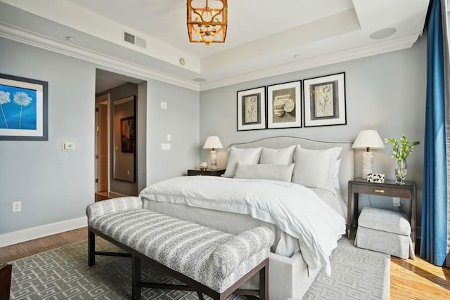 bedroom featuring a tray ceiling, wood finished floors, visible vents, baseboards, and a chandelier