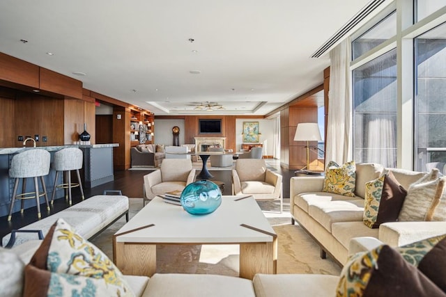 living room with ceiling fan, wood walls, wood finished floors, and a raised ceiling