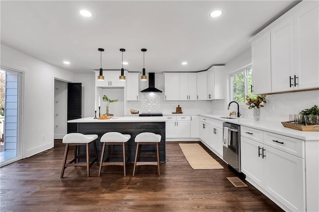 kitchen with stainless steel dishwasher, a kitchen island, wall chimney range hood, white cabinetry, and hanging light fixtures