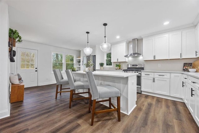 kitchen with stainless steel stove, white cabinets, hanging light fixtures, a center island, and wall chimney exhaust hood