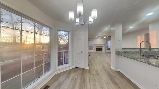 unfurnished dining area featuring a sink, wood finished floors, recessed lighting, a fireplace, and baseboards