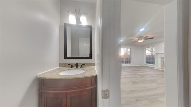 bathroom with vanity, wood finished floors, baseboards, a fireplace, and ceiling fan